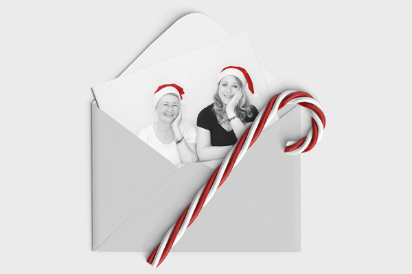 Titelbild der Dezember Edition des MASOMECO Magazins. Susanne und Britta mit Nikolausmützen auf dem Kopf lächeln auf einem Foto aus einem Briefumschlag, auf dem eine rot-weiße Zuckerstange liegt.